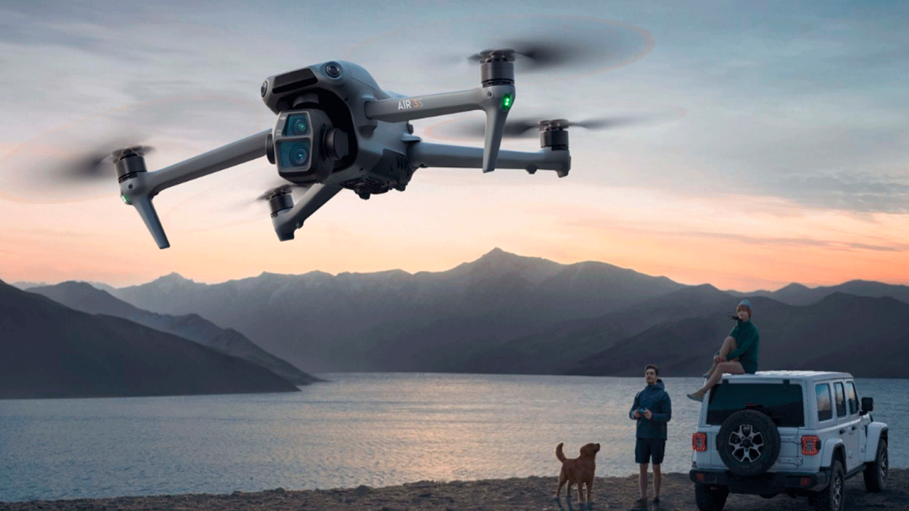 Дрон DJI Air 3S летит над озером в горах на закате, снимая людей, собаку и белый внедорожник на берегу на фоне живописного горного пейзажа