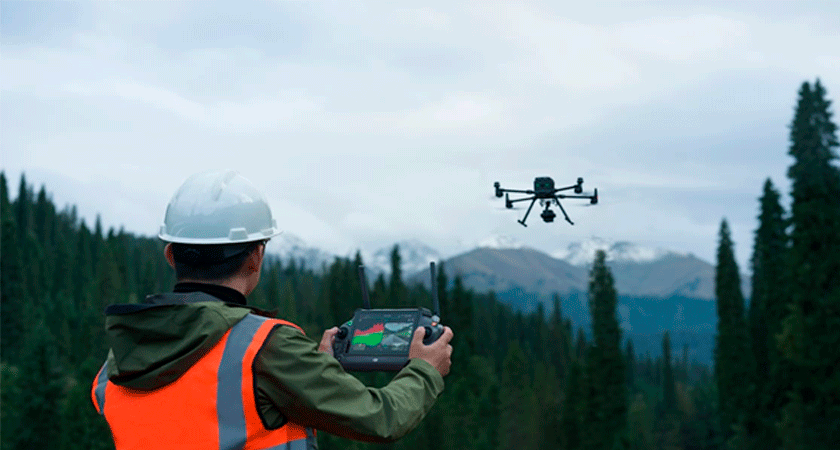 Оператор в каске и жилете управляет дроном с лидаром DJI Zenmuse L2 в горах и лесу