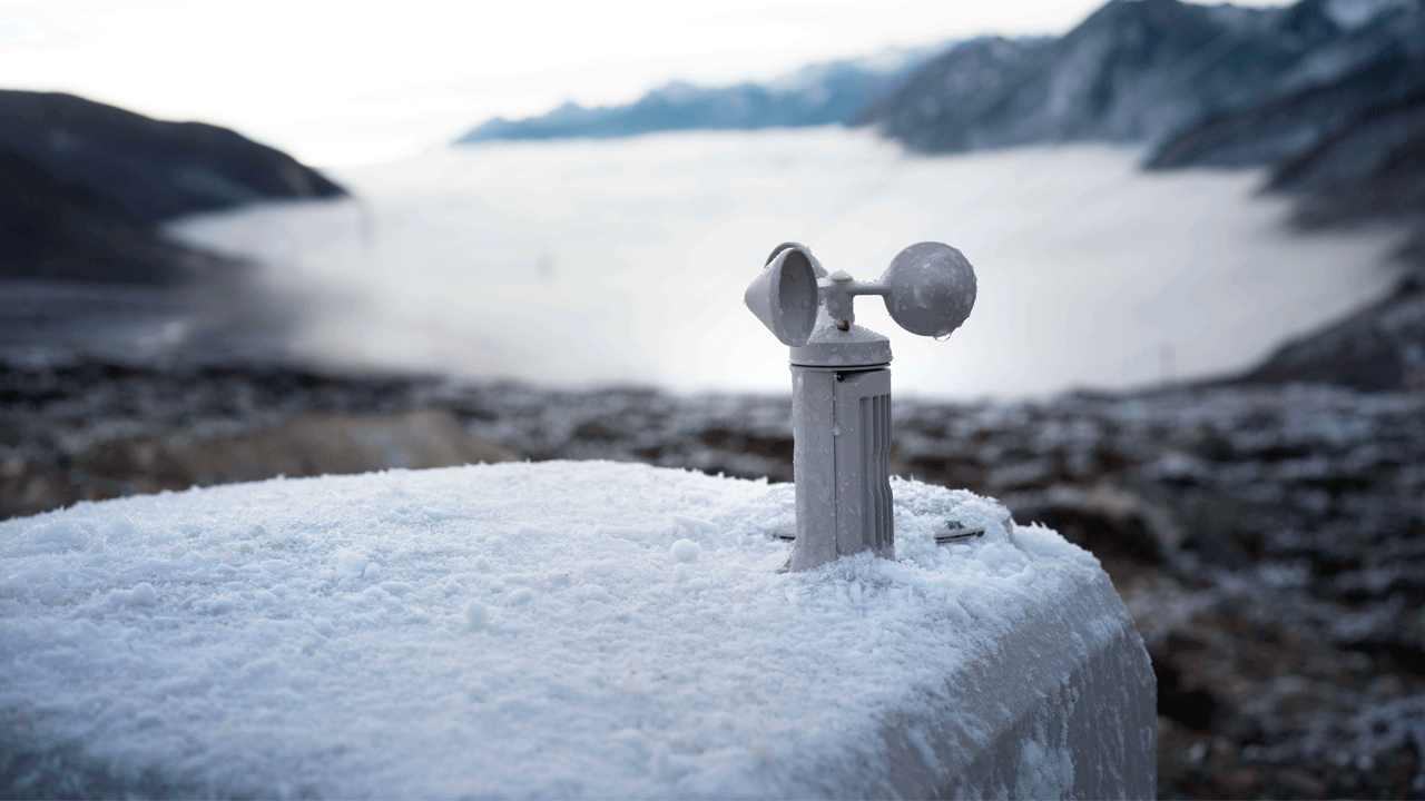 Док станция DJI Dock 3, установленная на заснеженной поверхности датчиком ветра на вершине. На заднем плане видны горы и туман в долине, демонстрирующие работу станции в экстремальных погодных условиях