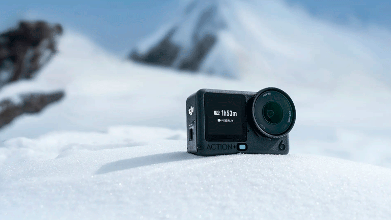 Экшн-камера DJI Osmo Action 6 стоит на снегу в горах, демонстрируя морозоустойчивость и длительное время работы.